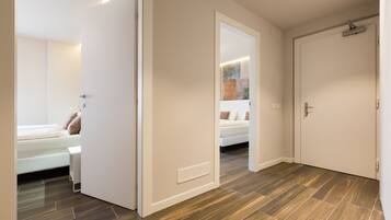 A modern hotel room with a bed, bedside table, and a door leading to another room.