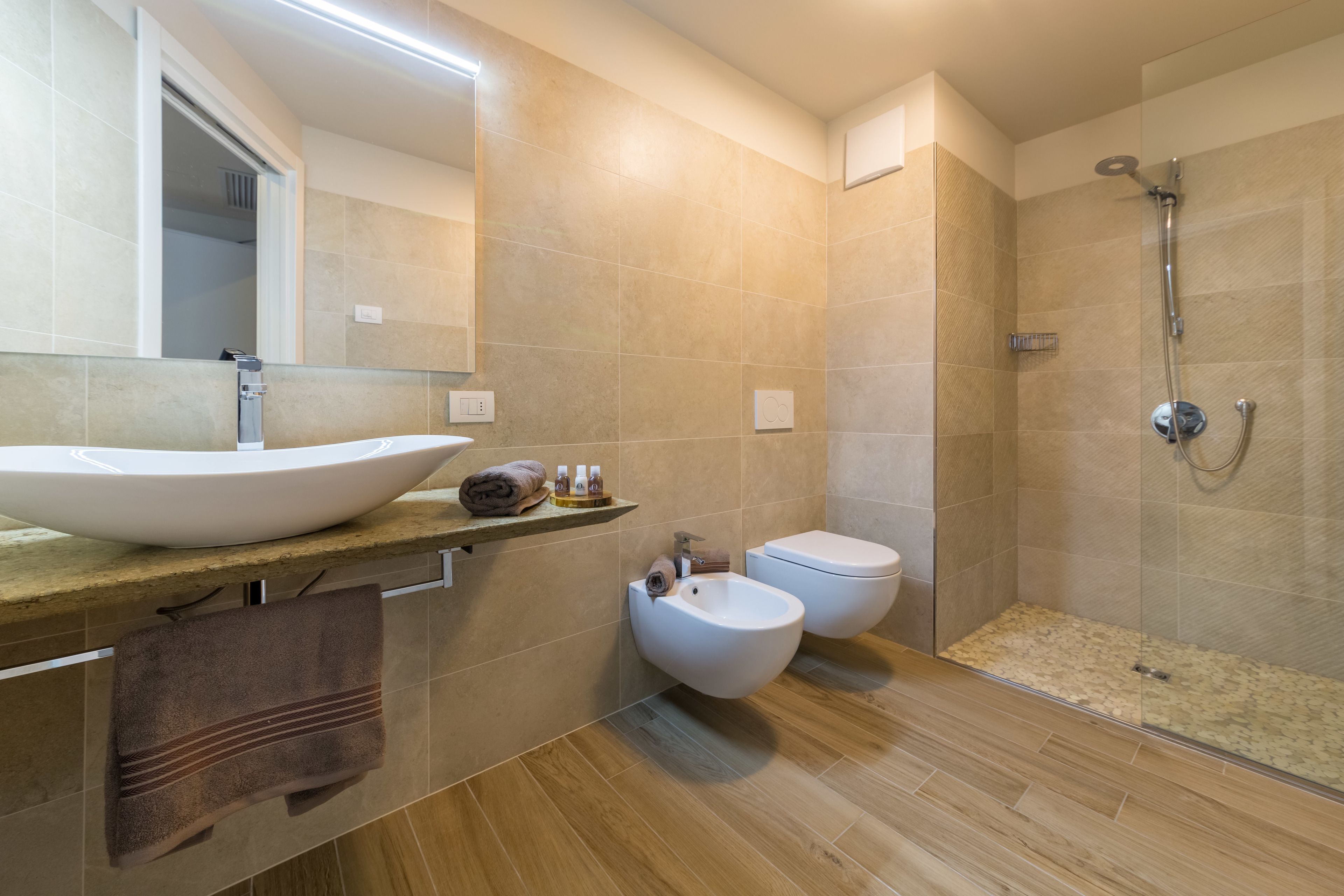 Ein modernes Badezimmer mit einem großen Waschbecken, Bidet und einer behindertzugänglichen Glasdusche.