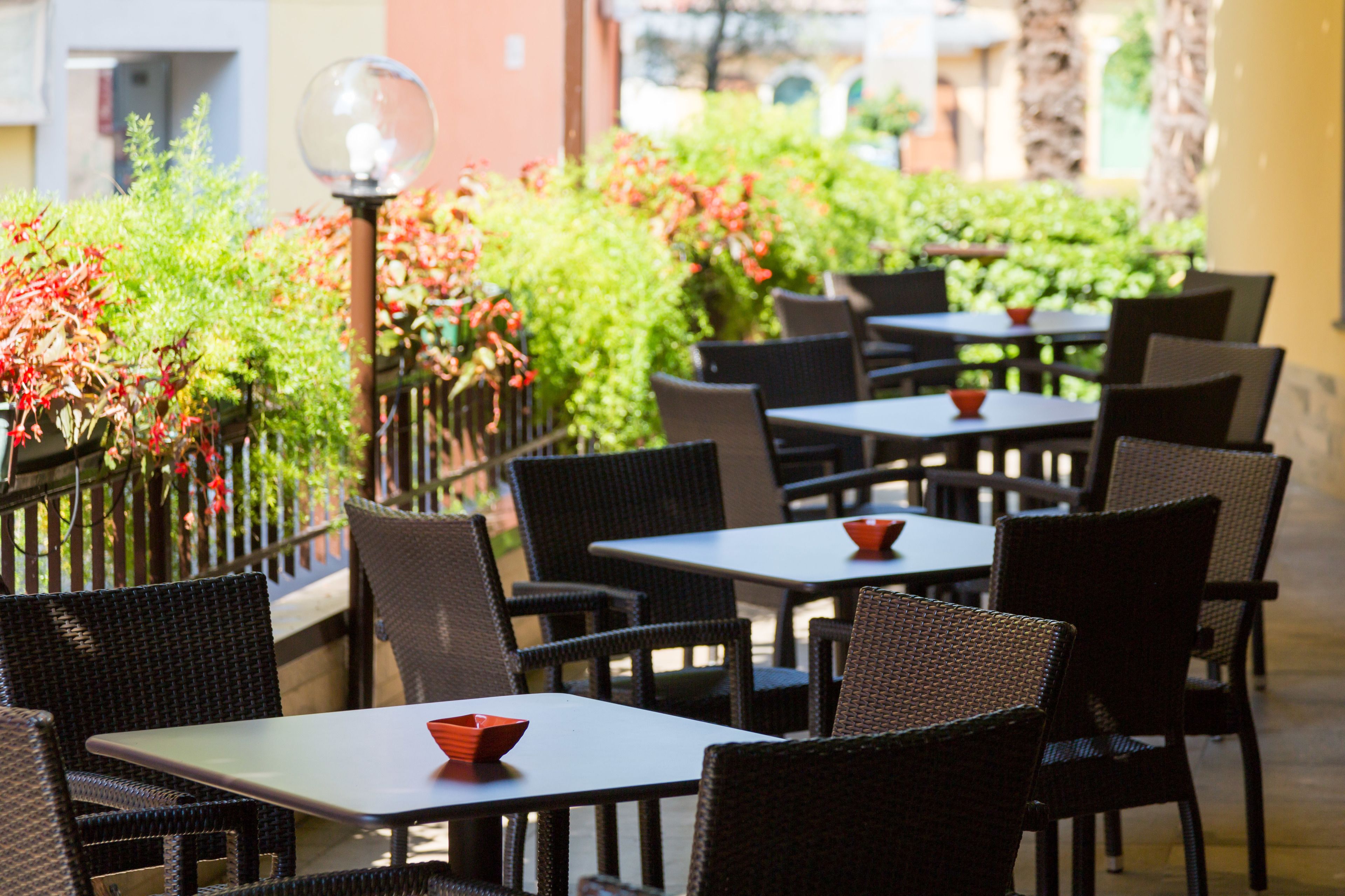 An outdoor seating area with wicker tables and chairs, surrounded by greenery and a decorative lamp post.