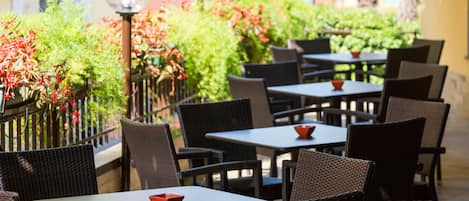 An outdoor seating area with wicker tables and chairs, surrounded by greenery and a decorative lamp post.