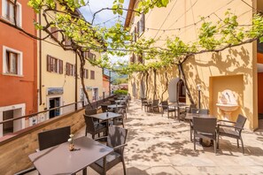 An outdoor café with tables and chairs, surrounded by buildings with vines and a fountain. - PACE 1954 Hotel (Arco)