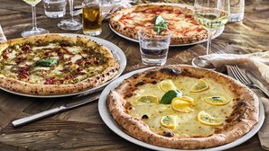 Een restauranttafel met drie pizza's, wijnglazen en een waterfles.