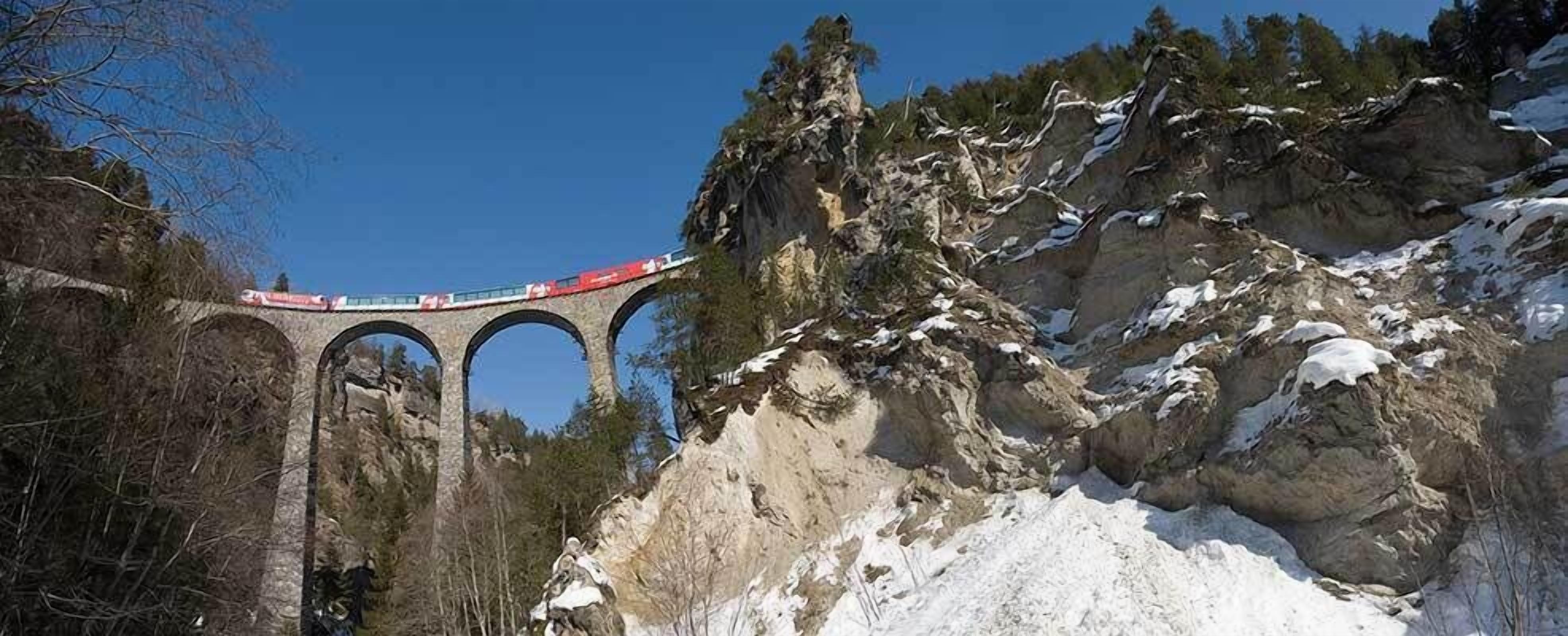 Un train traverse un pont de pierre au-dessus d’une montagne enneigée.
