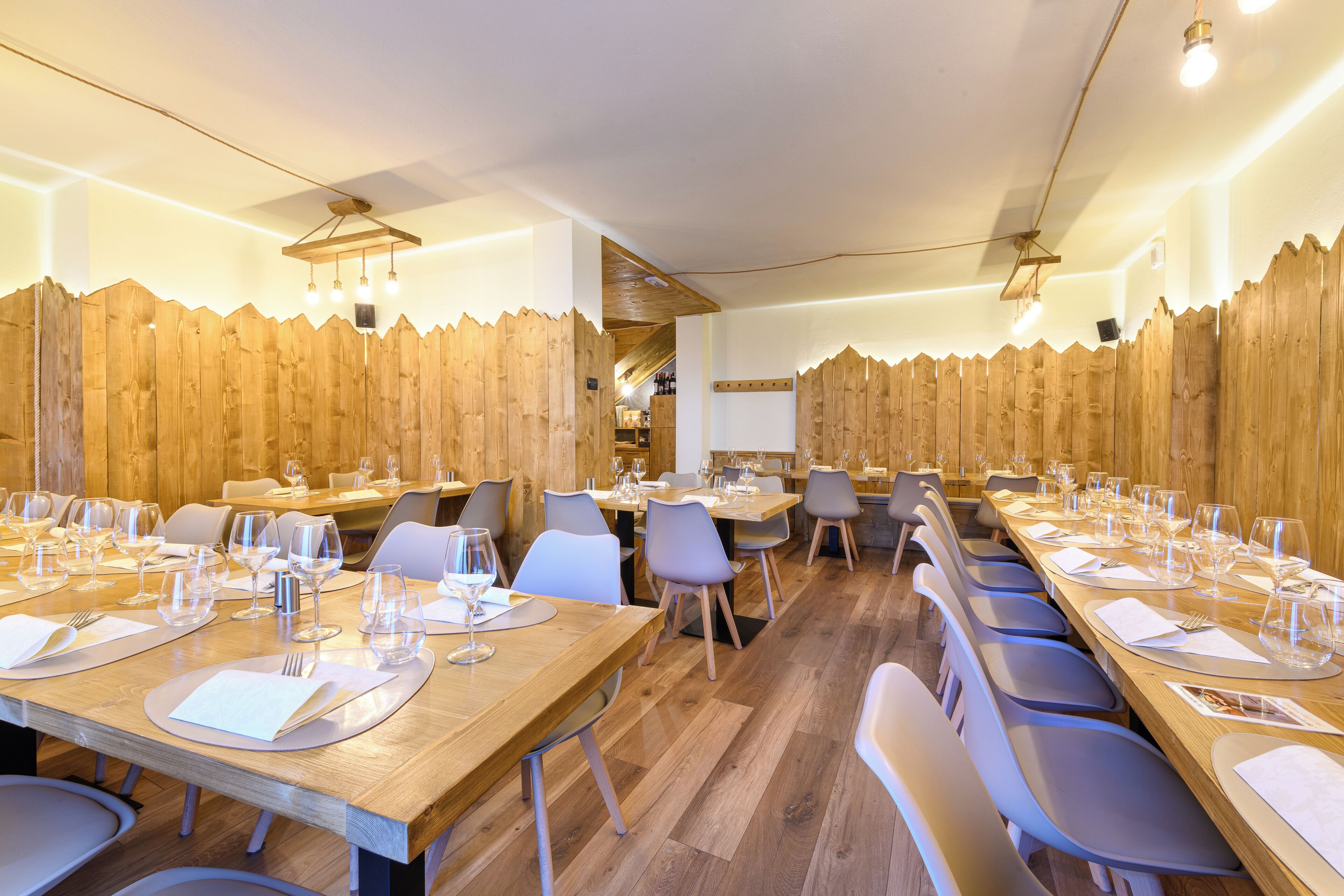 Un restaurante con paneles de madera, varias mesas dispuestas con manteles blancos y sillas modernas.