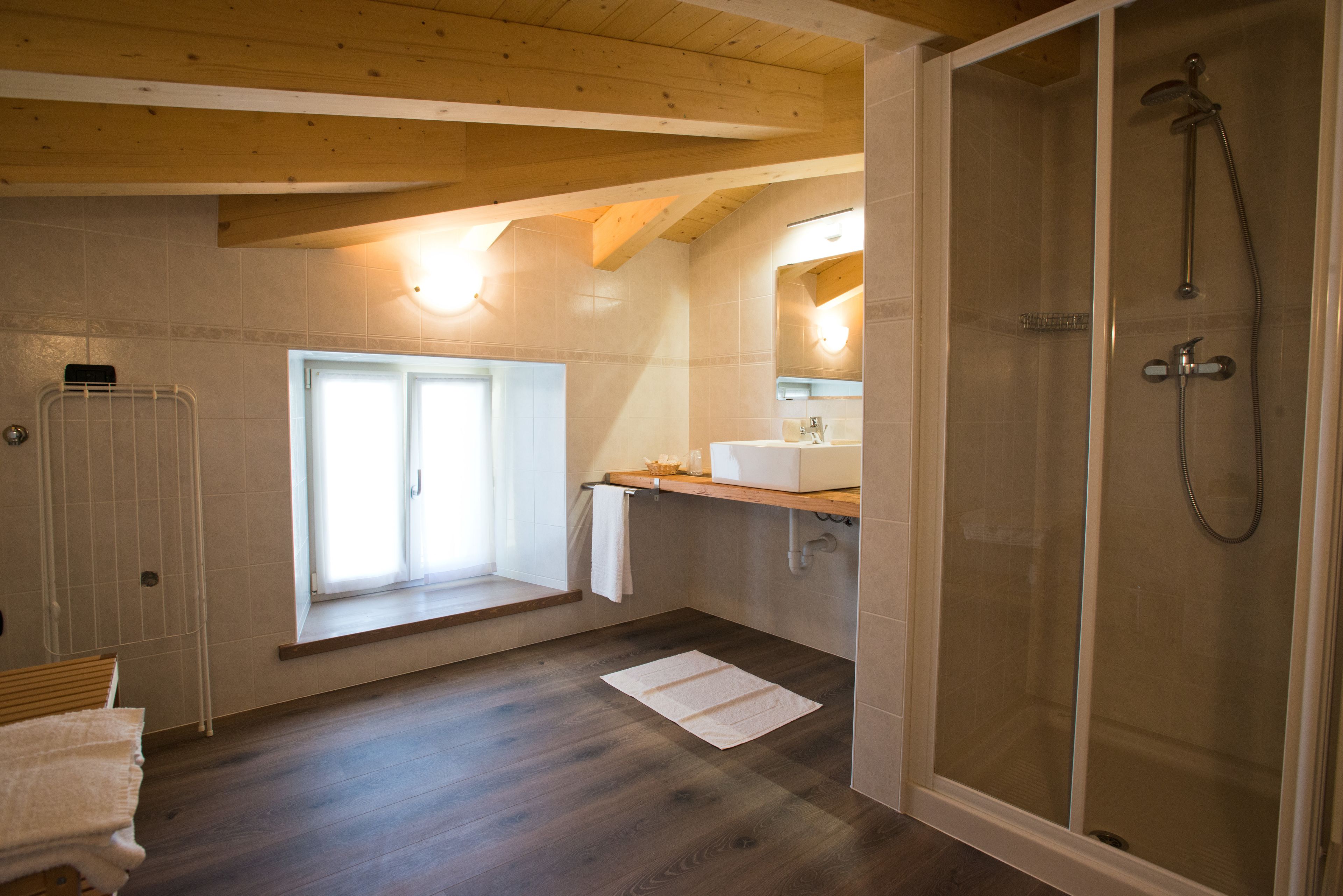 A bathroom with a wooden ceiling, a window, a shower, and a sink.