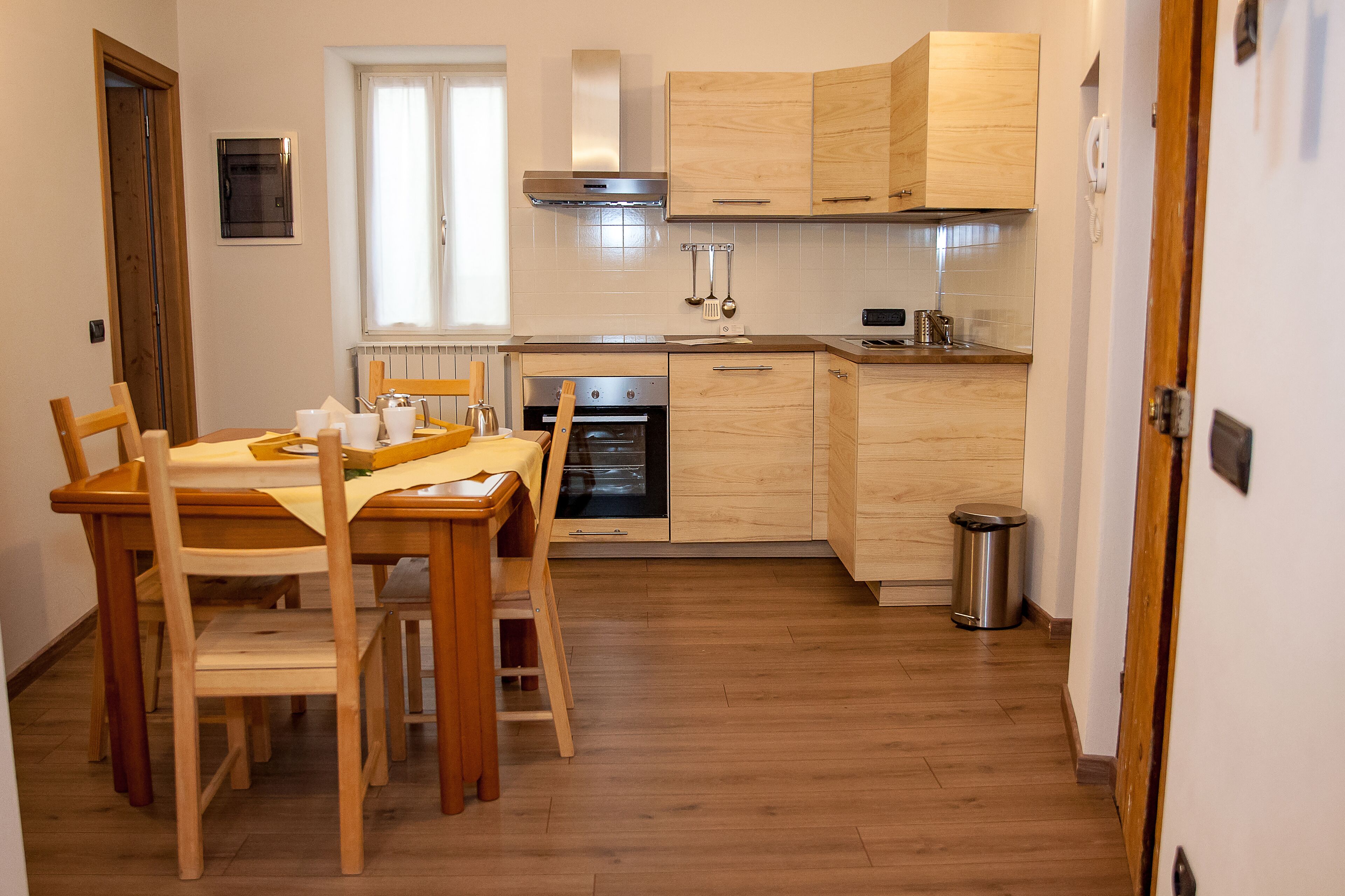 Eine kleine Küche mit Holzschränken, einem eingebauten Backofen und einem Esstisch mit Stühlen.