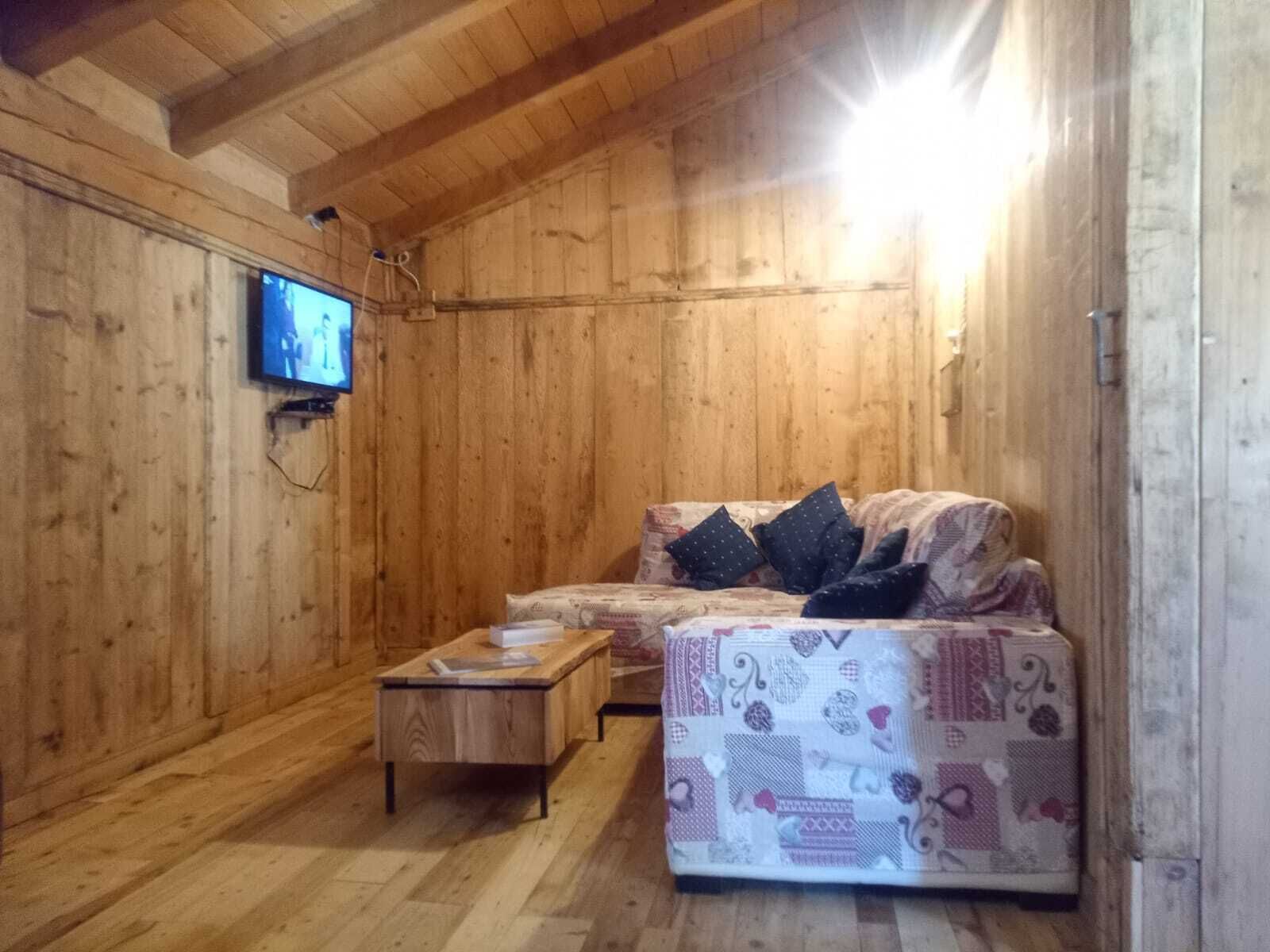 Een gezellig houten vertrek met een bank, een klein houten tafeltje en een aan de muur bevestigde televisie.