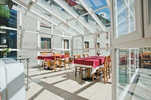 Un comedor iluminado por el sol con mesas y sillas, ventanas amplias y vistas al exterior.