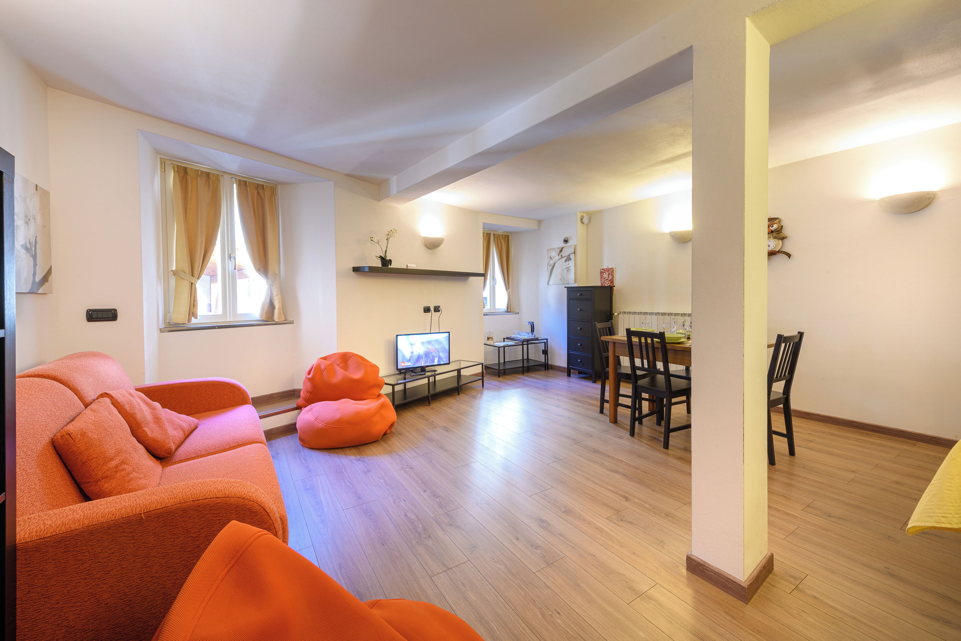 Een moderne woonkamer met een bank, een televisie en een eethoek met stoelen en een tafel.