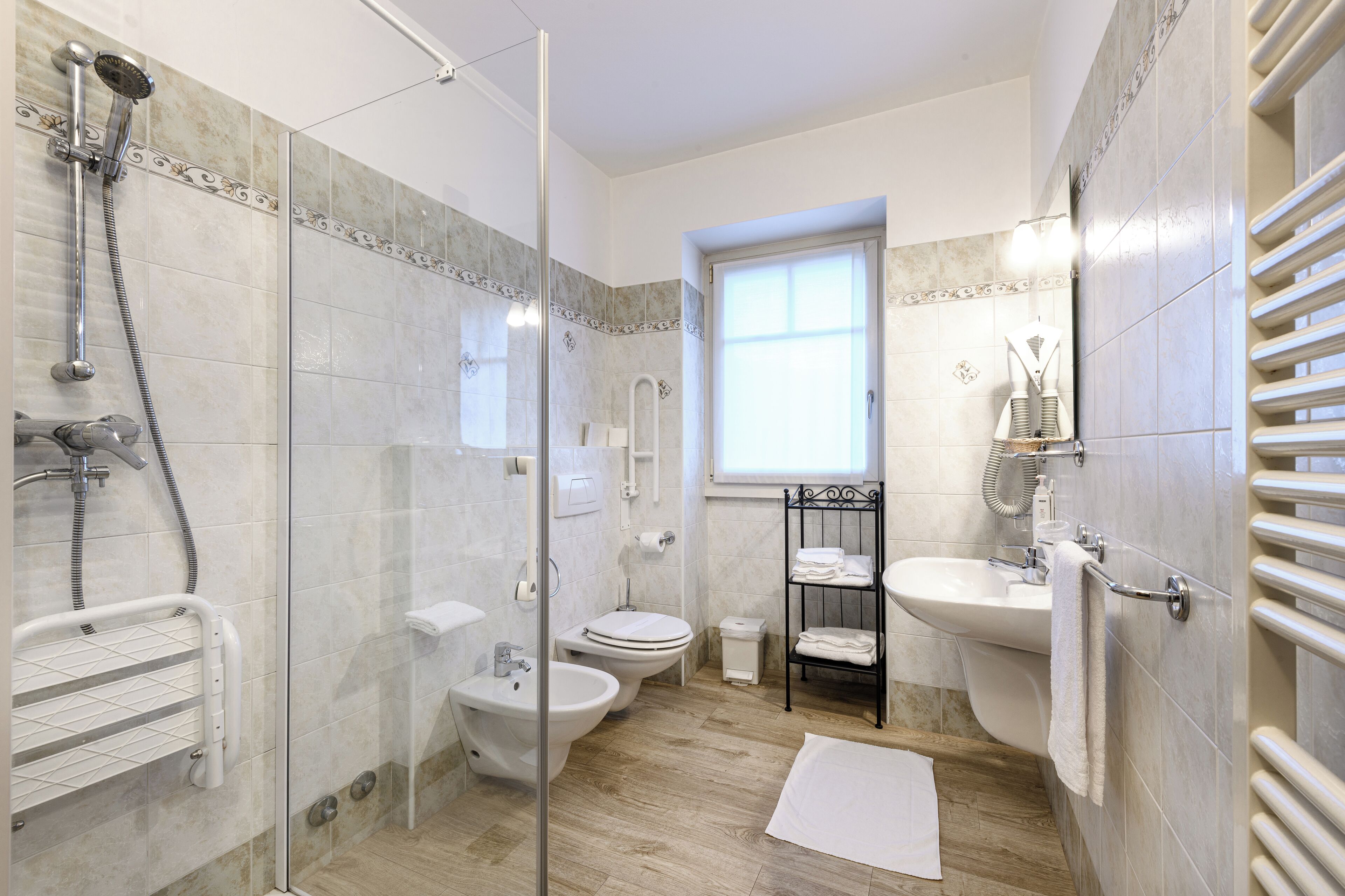 A bathroom with a glass-enclosed shower, a bidet, a toilet, a sink, and a towel rack.