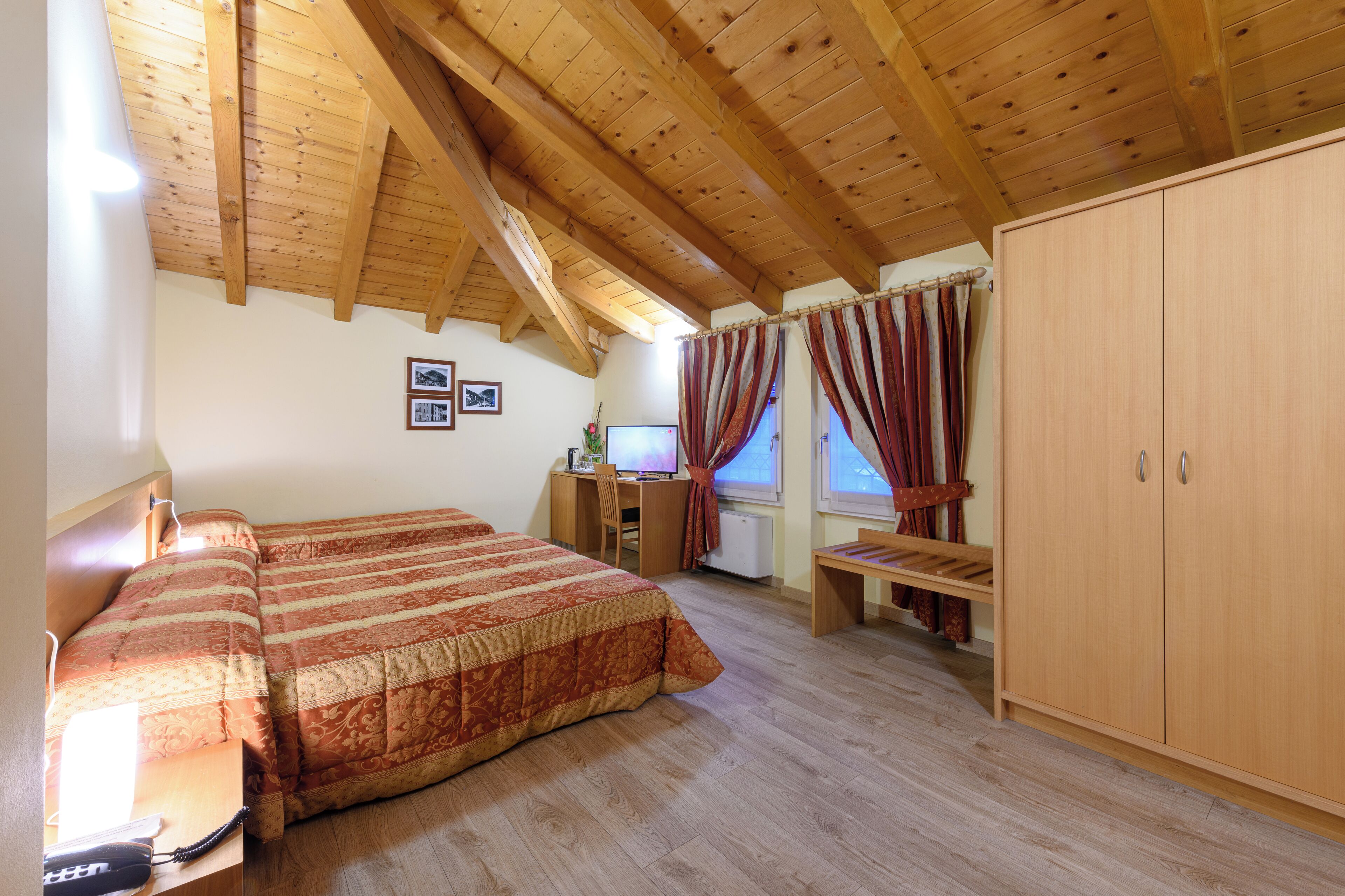 A bedroom with a wooden ceiling, a large bed, a desk with a computer, and a wardrobe.