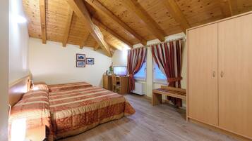 A bedroom with a wooden ceiling, a large bed, a desk with a computer, and a wardrobe.