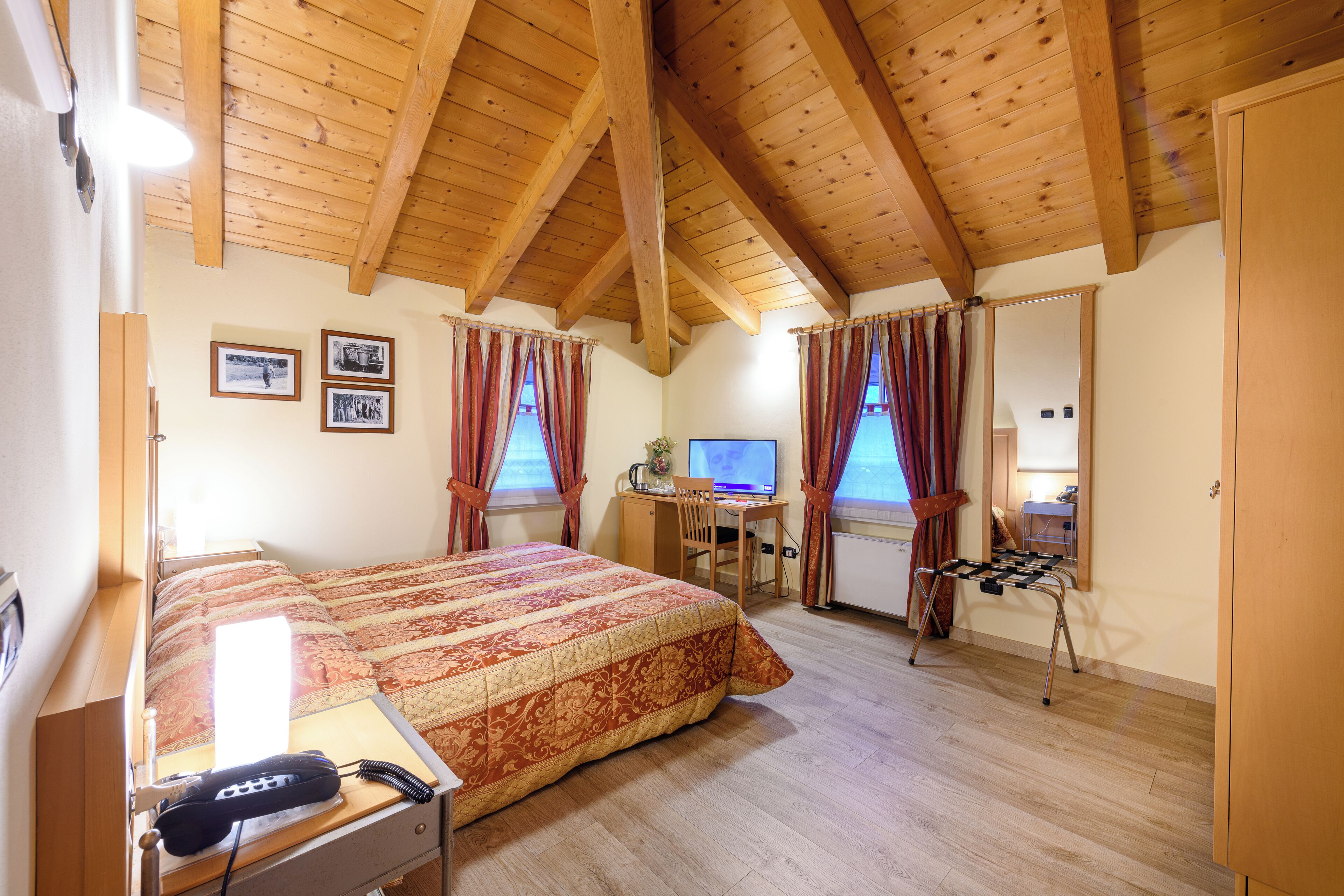 A bedroom with a wooden ceiling, a bed with a patterned bedspread, a desk with a computer, and a chair.