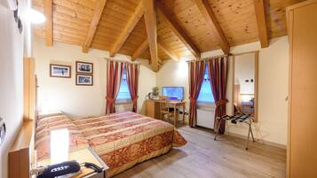A bedroom with a wooden ceiling, a bed with a patterned bedspread, a desk with a computer, and a chair.