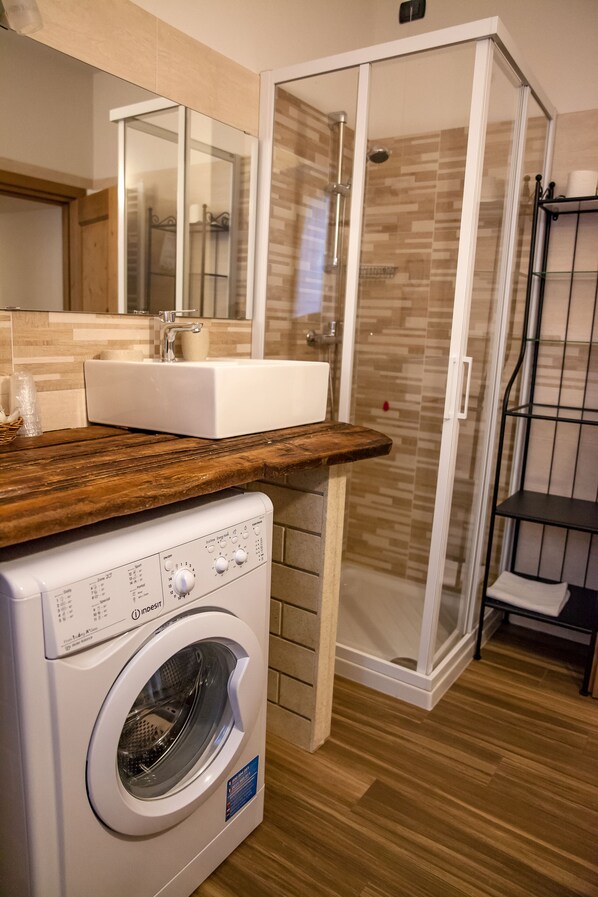Un baño pequeño con lavadora, lavamanos y cabina de ducha.