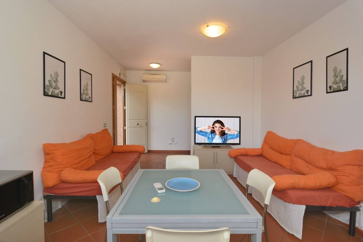 A compact living space with two orange sofas, a small dining table, a television, and a microwave.