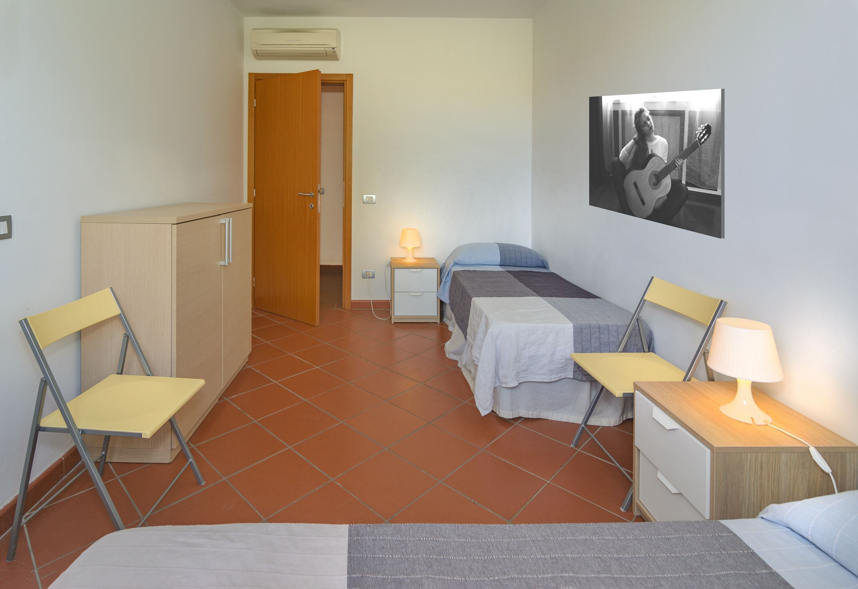 A compact hotel room with a bed, two bedside tables with lamps, a chair, a wardrobe, and a picture on the wall.