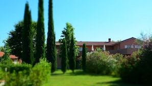 A residential building with a red-tiled roof, surrounded by lush greenery and tall trees.