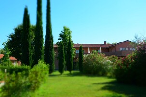 A residential building with a red-tiled roof, surrounded by lush greenery and tall trees.