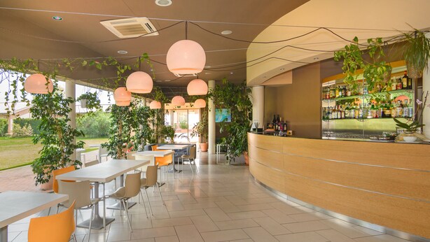 A modern cafe with outdoor seating, a bar area, and abundant greenery.