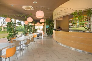 A modern cafe with outdoor seating, a bar area, and abundant greenery.