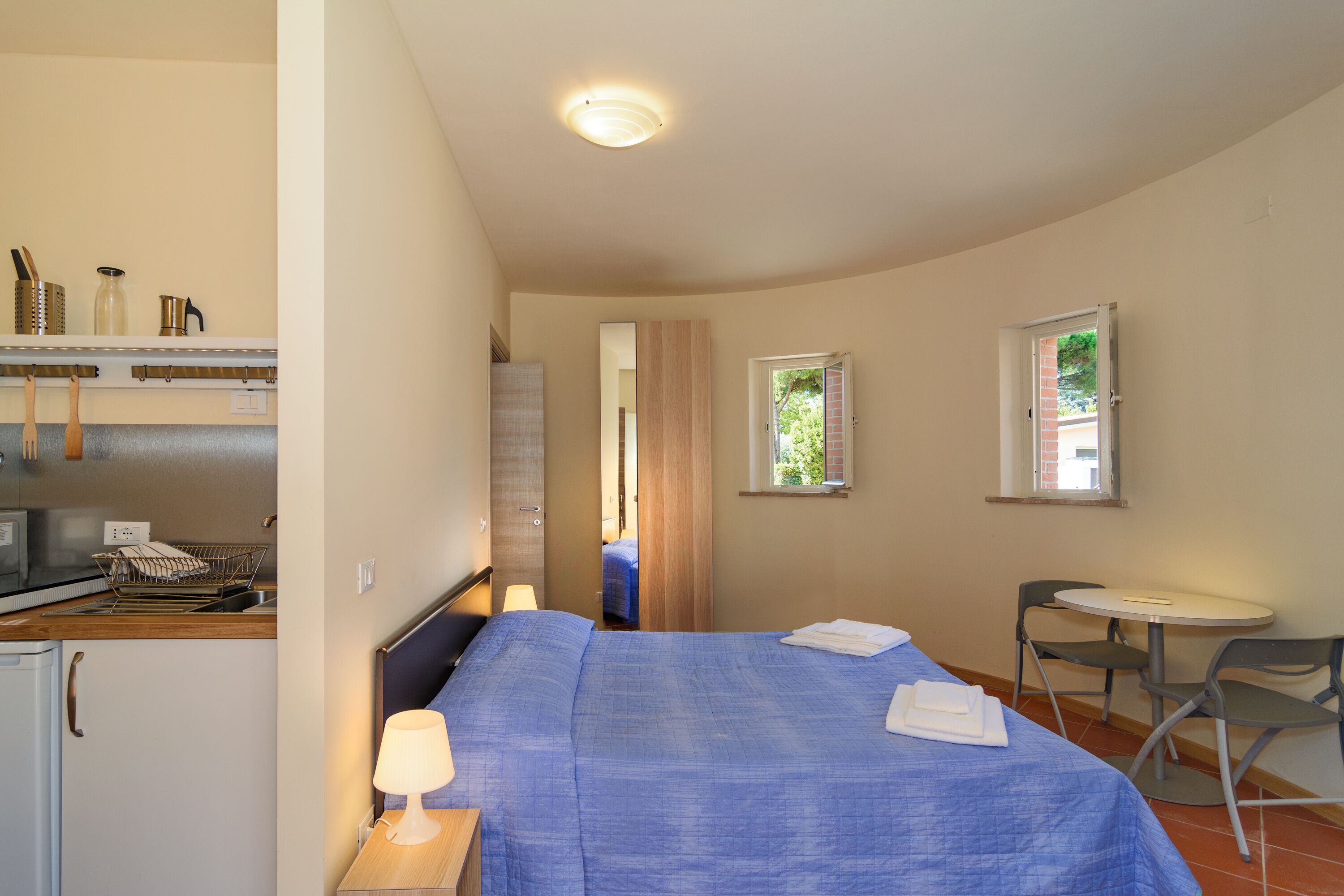 A bedroom with a bed, bedside table, lamp, and a small table with chairs.