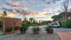 A paved courtyard with potted plants, a brick building, and a parked car.