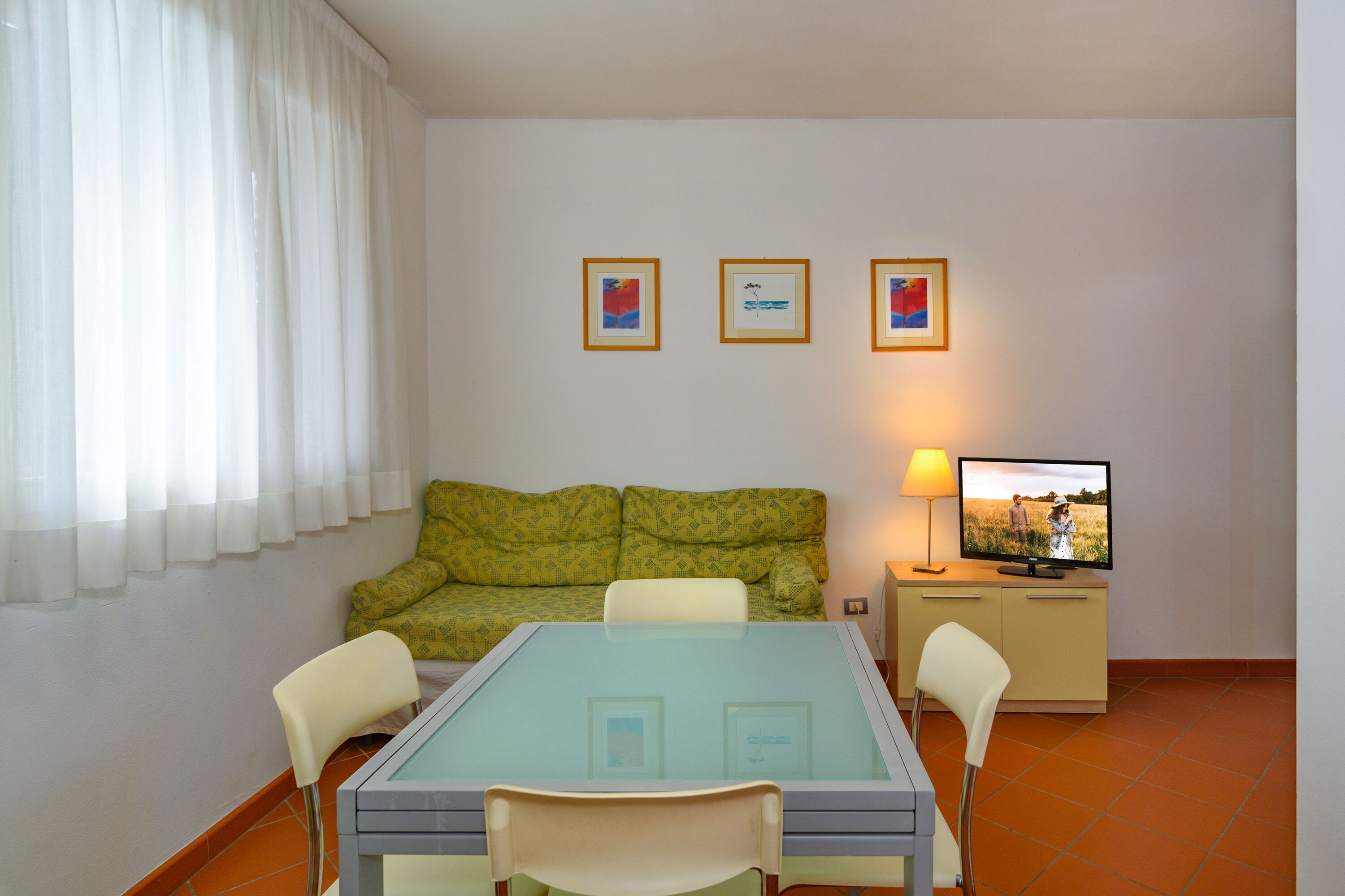 Une pièce comprenant une table à plateau en verre, deux chaises, un canapé, un téléviseur et des tableaux encadrés accrochés au mur.