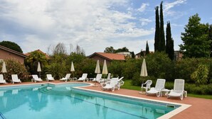 A swimming pool with white lounge chairs and umbrellas, surrounded by greenery and buildings.
