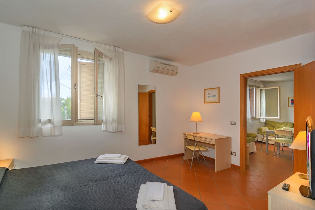 A hotel room with a bed, a desk, a chair, a lamp, and a TV.
