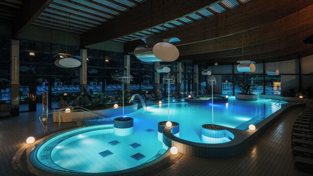 A modern indoor swimming pool with a wooden ceiling, large windows, and contemporary lighting fixtures. - Hotel Balnea Superior – Terme Krka (Dolenjske Toplice)