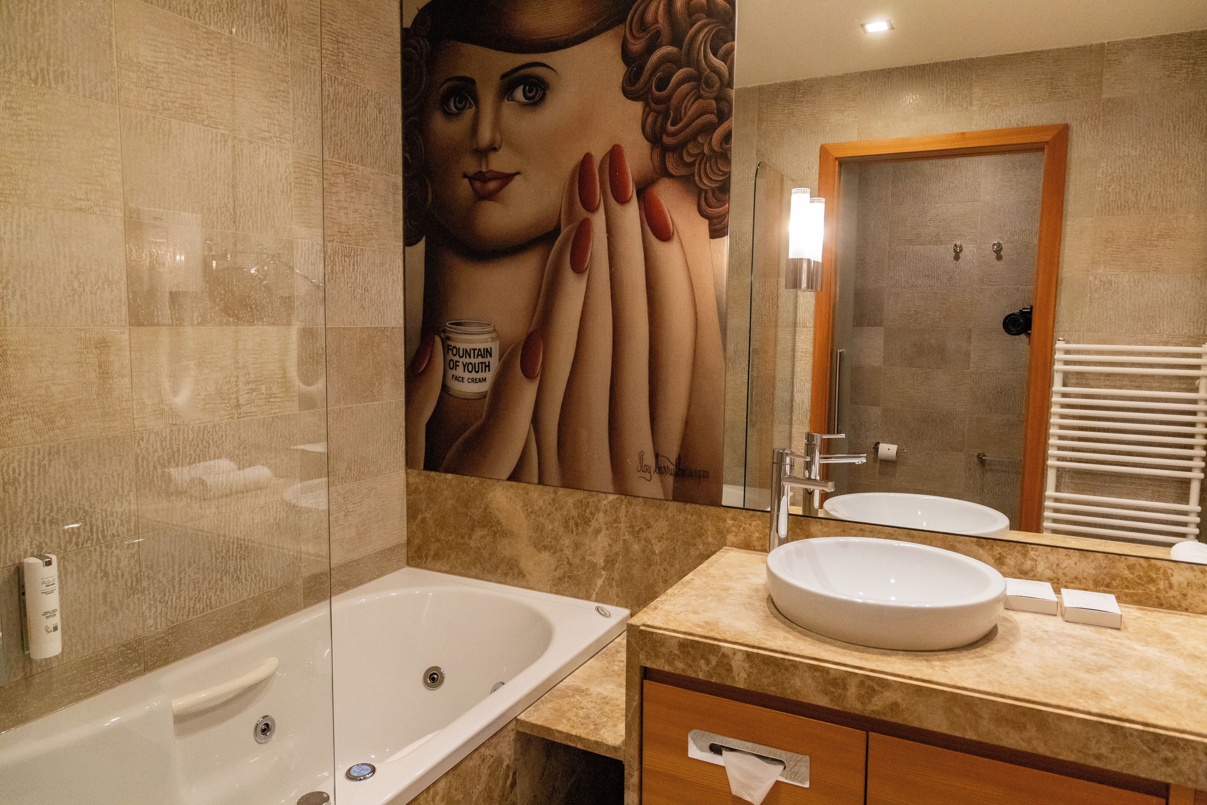 A bathroom with a bathtub, a sink, a mirror, and a large wall mural.
