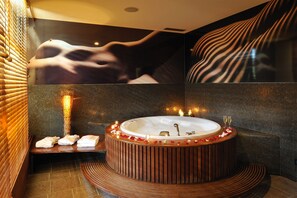 A modern bathroom with a round wooden bathtub, a glass shower enclosure, and a mosaic wall.
