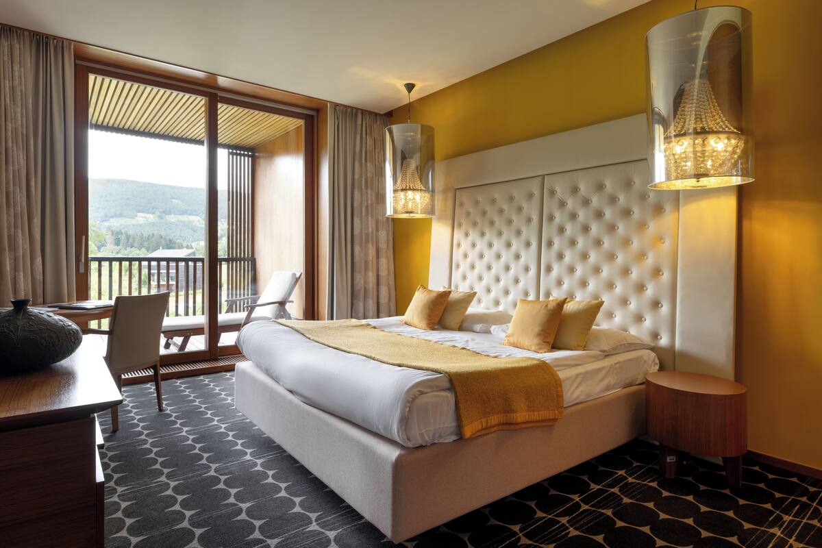 A hotel room with a large bed, a desk, a chair, and a balcony with a view.