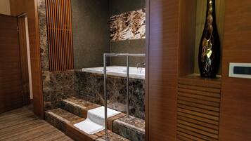 A modern bathroom with a marble-tiled shower, a glass-enclosed bathtub, and a wooden door.