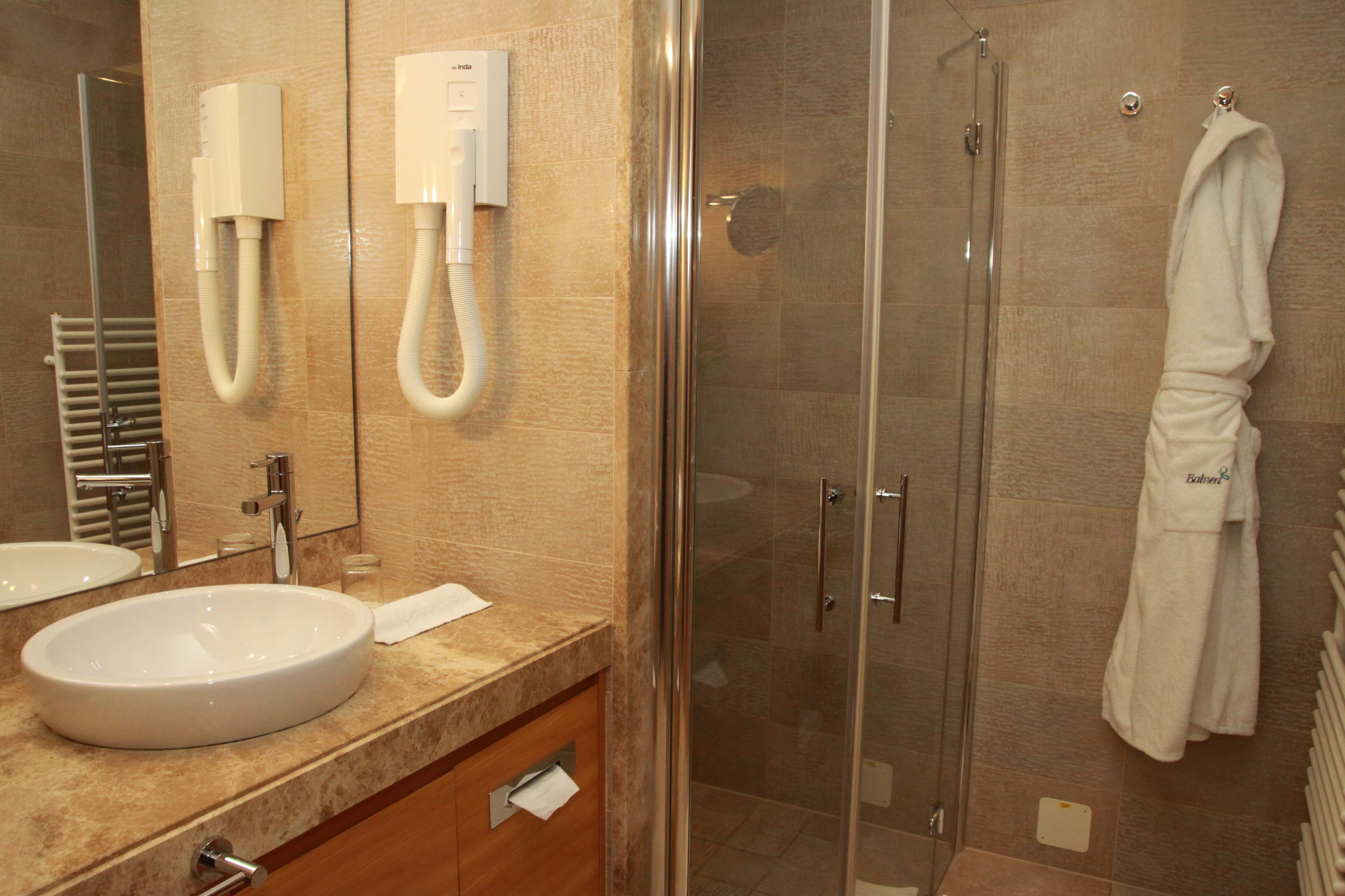 Un baño con lavamanos, espejo, toallero y cabina de ducha de vidrio.