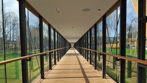 A corridor with large windows on both sides, leading to a distant view of a park and trees. - Hotel Balnea Superior – Terme Krka (Dolenjske Toplice)