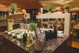 Un área de bufé con diversos platos de comida, botellas de condimentos y plantas en macetas.