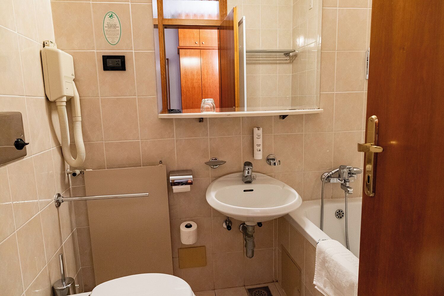 Een kleine badkamer met toilet, wastafel en douche. Handdoekhouder, spiegel en een plank boven de wastafel aanwezig.