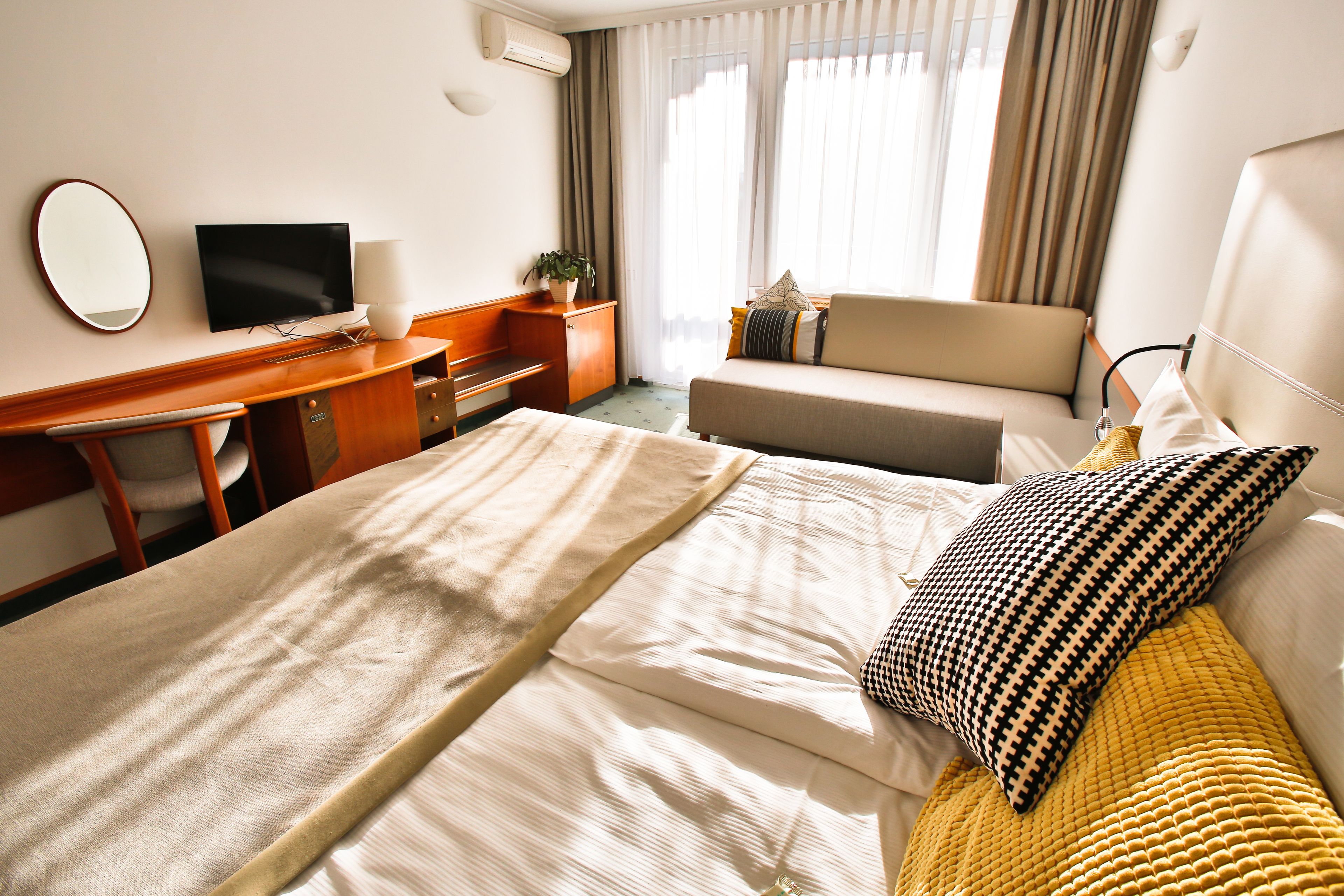 A hotel room with a bed, a desk, a chair, a television, and a window with curtains.