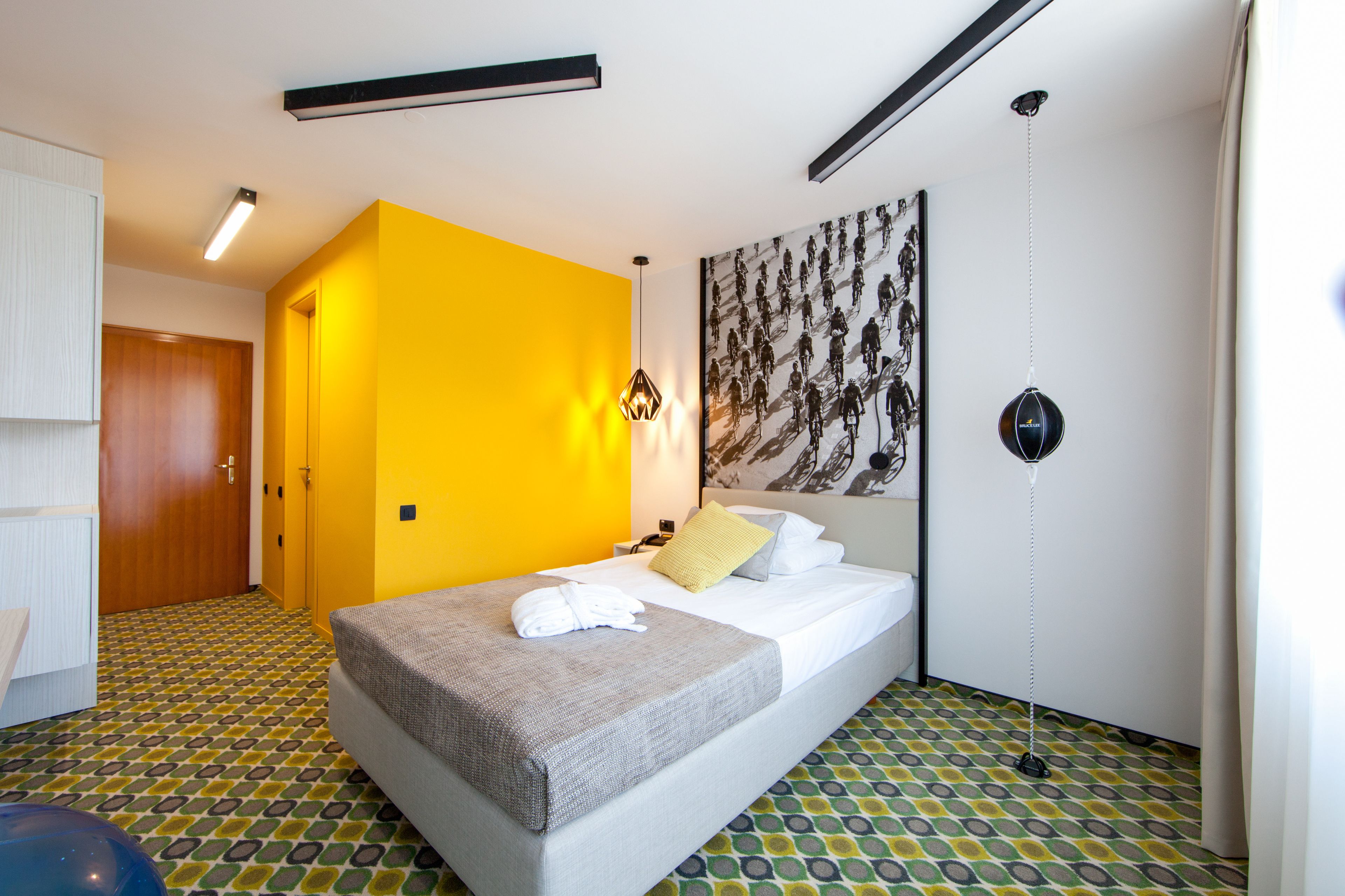 Une chambre d’hôtel avec un lit, un mur d’accent jaune, un sol à motifs et une grande œuvre d’art accrochée au mur.