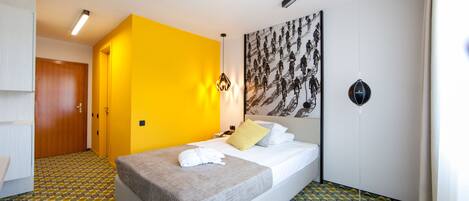 Une chambre d’hôtel avec un lit, un mur d’accent jaune, un sol à motifs et une grande œuvre d’art accrochée au mur.