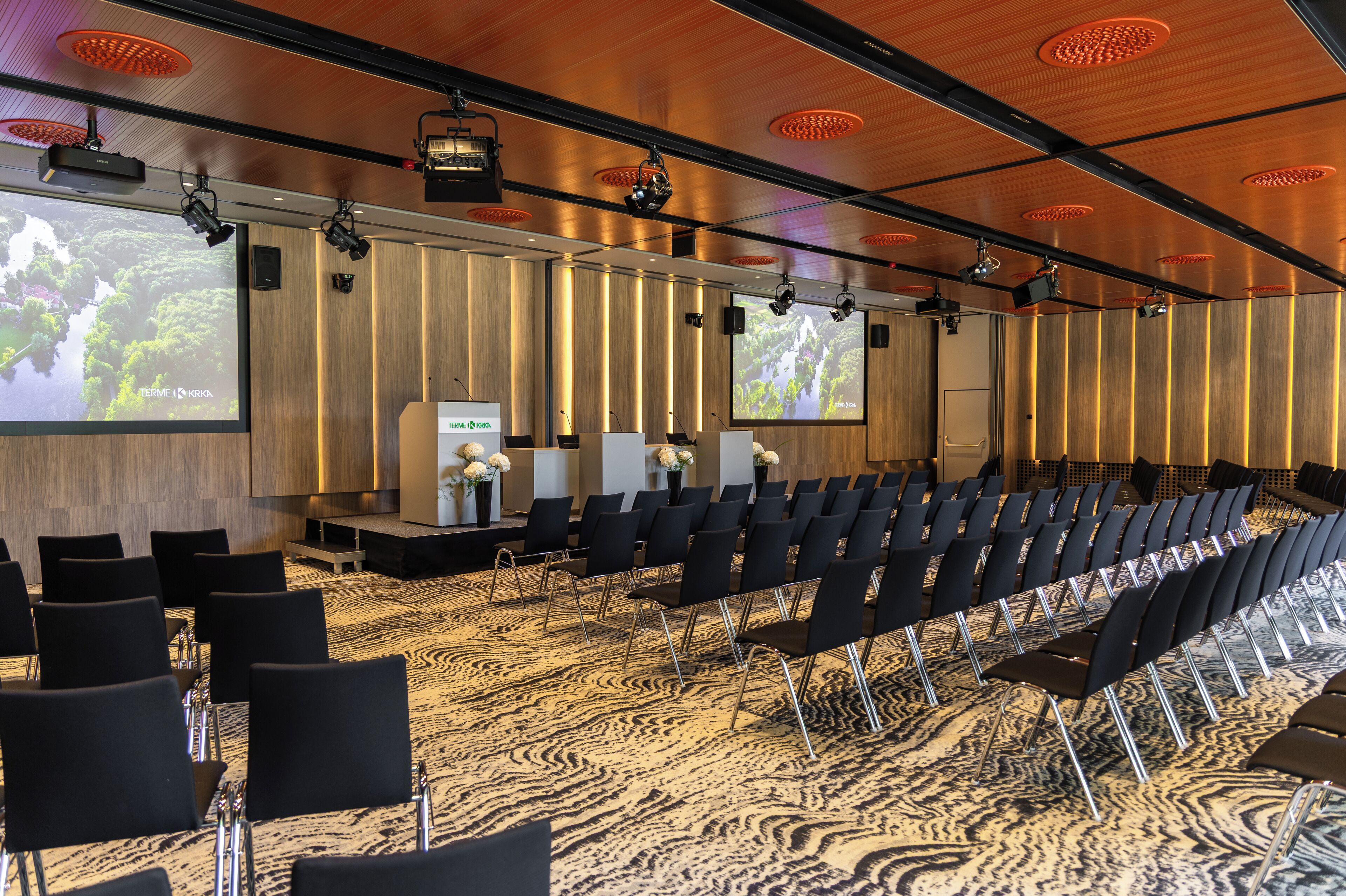 A conference room with rows of chairs, a large screen, and a podium.
