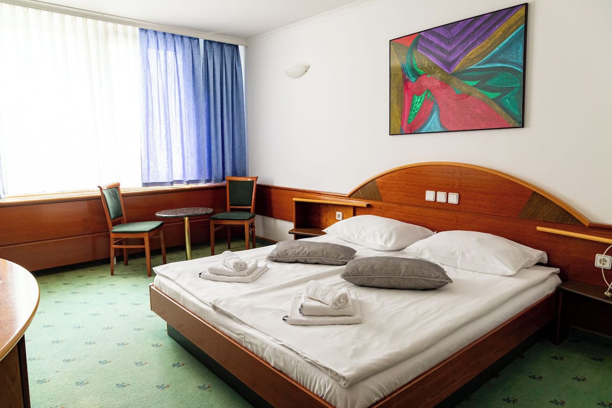 A hotel room with a bed, a chair, a desk, and a window with curtains.