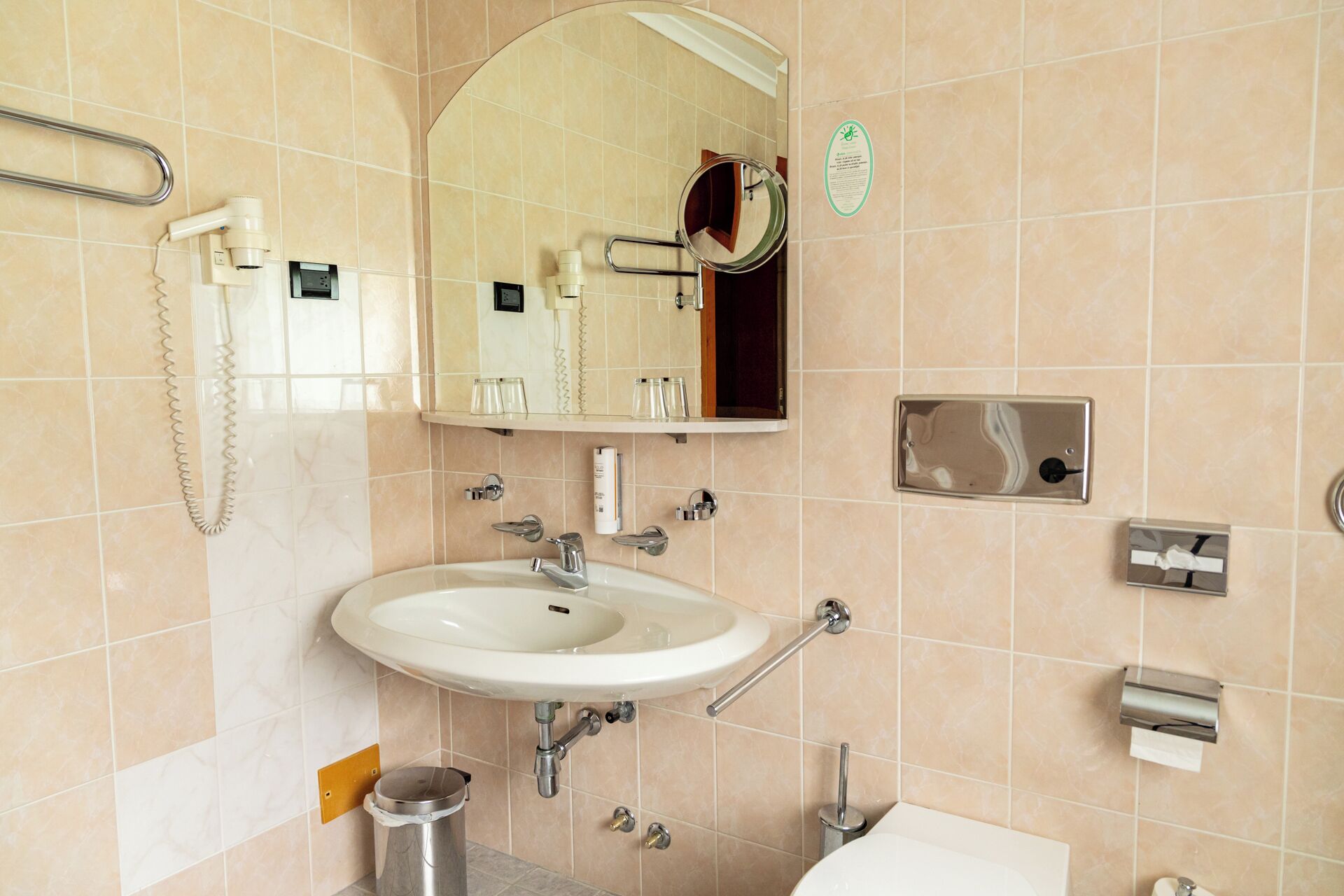 Une salle de bain équipée d’un lavabo, d’un miroir, d’un porte-serviettes et d’un sèche-mains.