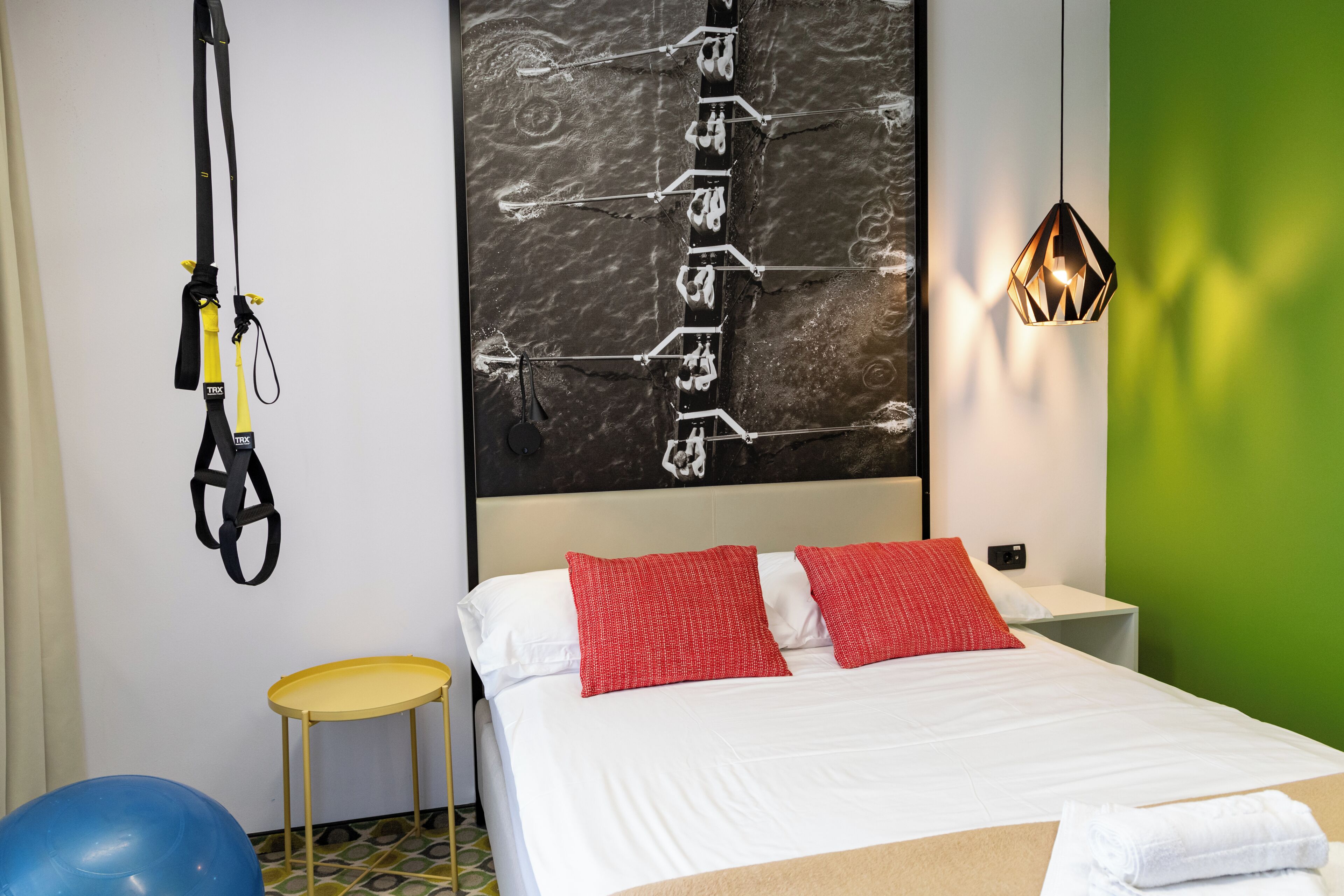 Habitación de hotel moderna con cama, equipo de ejercicios, una mesita y una pared de acento verde.