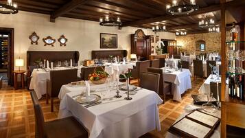 A restaurant with multiple tables set for dining, featuring white tablecloths, candles, and a variety of dishes.