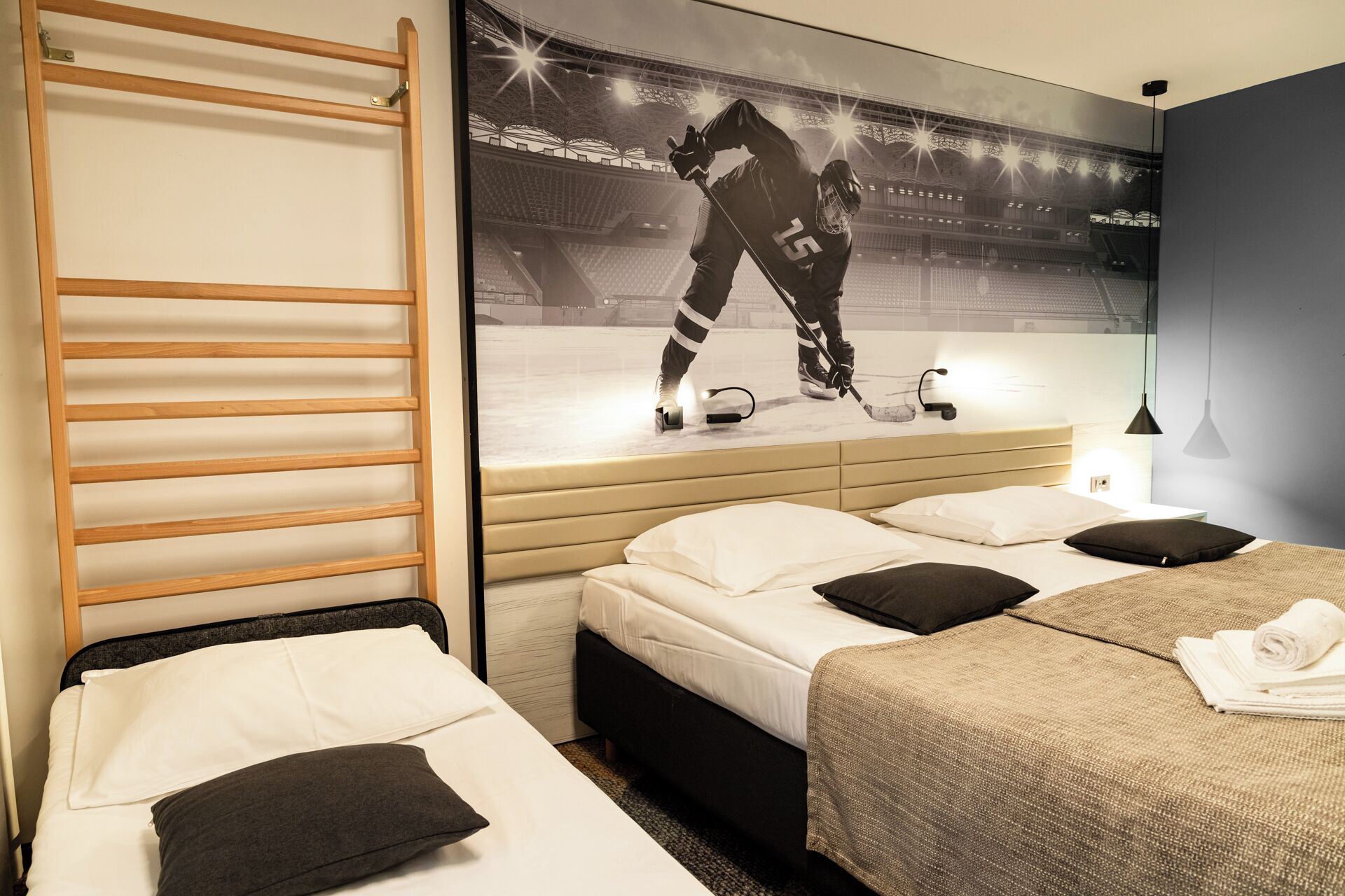 A hotel room with two beds, a wooden ladder, a hockey player on the wall, and a nightstand with a lamp.