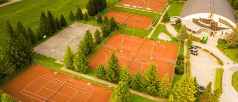 Vista aérea de un complejo deportivo con varias canchas de tenis, un estacionamiento y un edificio grande con cúpula.