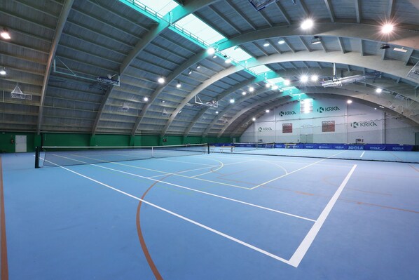 An indoor tennis court with a high ceiling and multiple overhead lights.